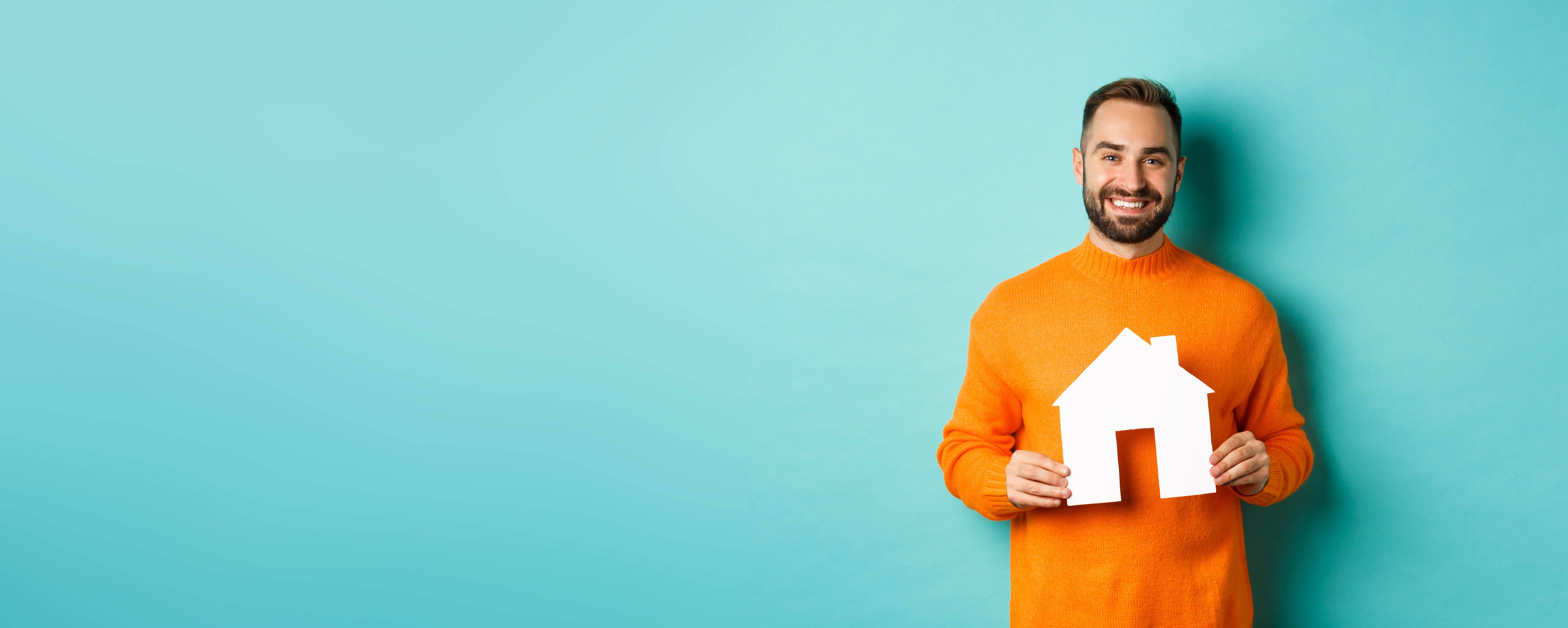 real estate concept. happy young man searching for home rent, holding house paper maket and smiling, standing over blue background
